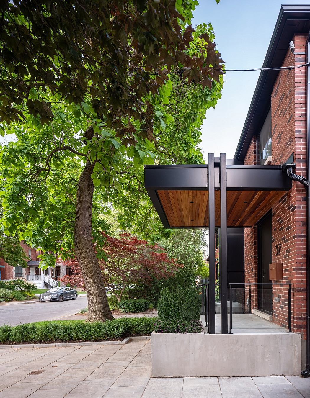 Modern awning over a brick building's entrance, surrounded by greenery.