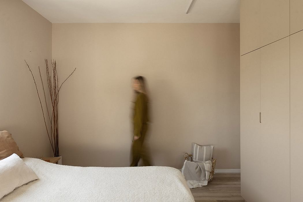 Minimalist bedroom with blurred person walking, neutral tones, and simple decor.