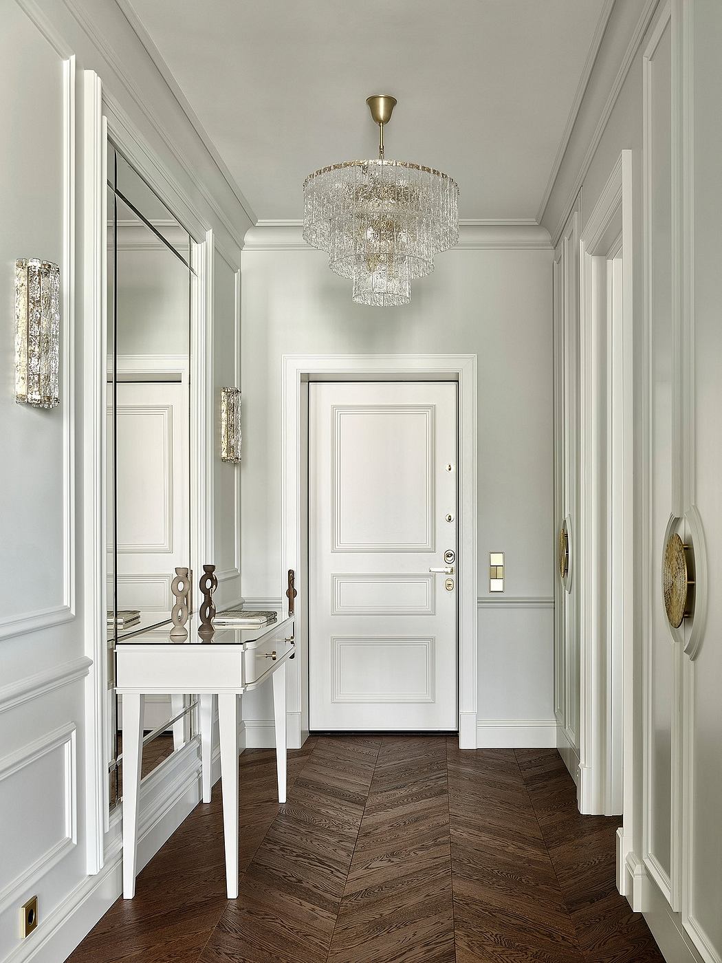 Elegant entryway with a crystal chandelier, herringbone flooring, and decorative moldings.