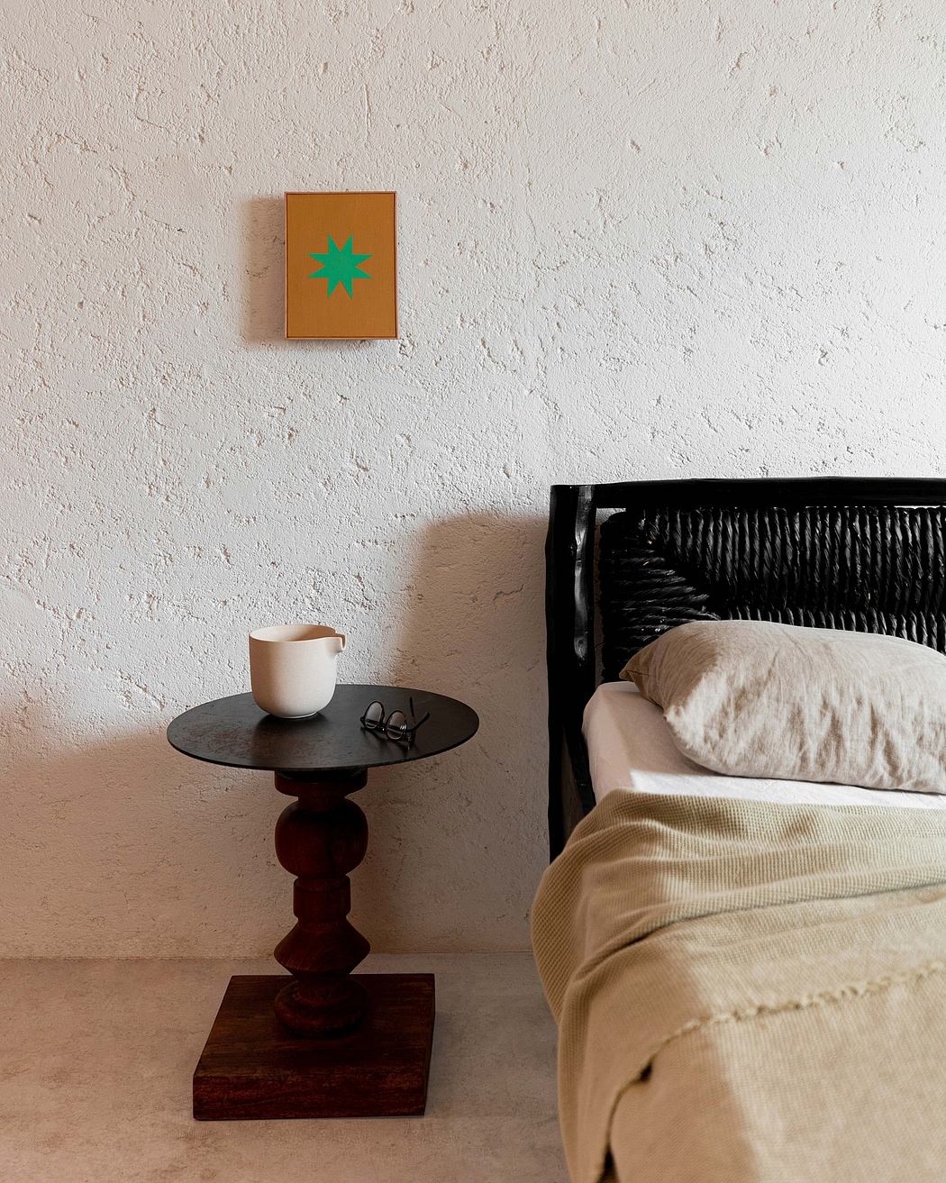 Simple bedroom corner with a round table, mug, and framed art on wall.