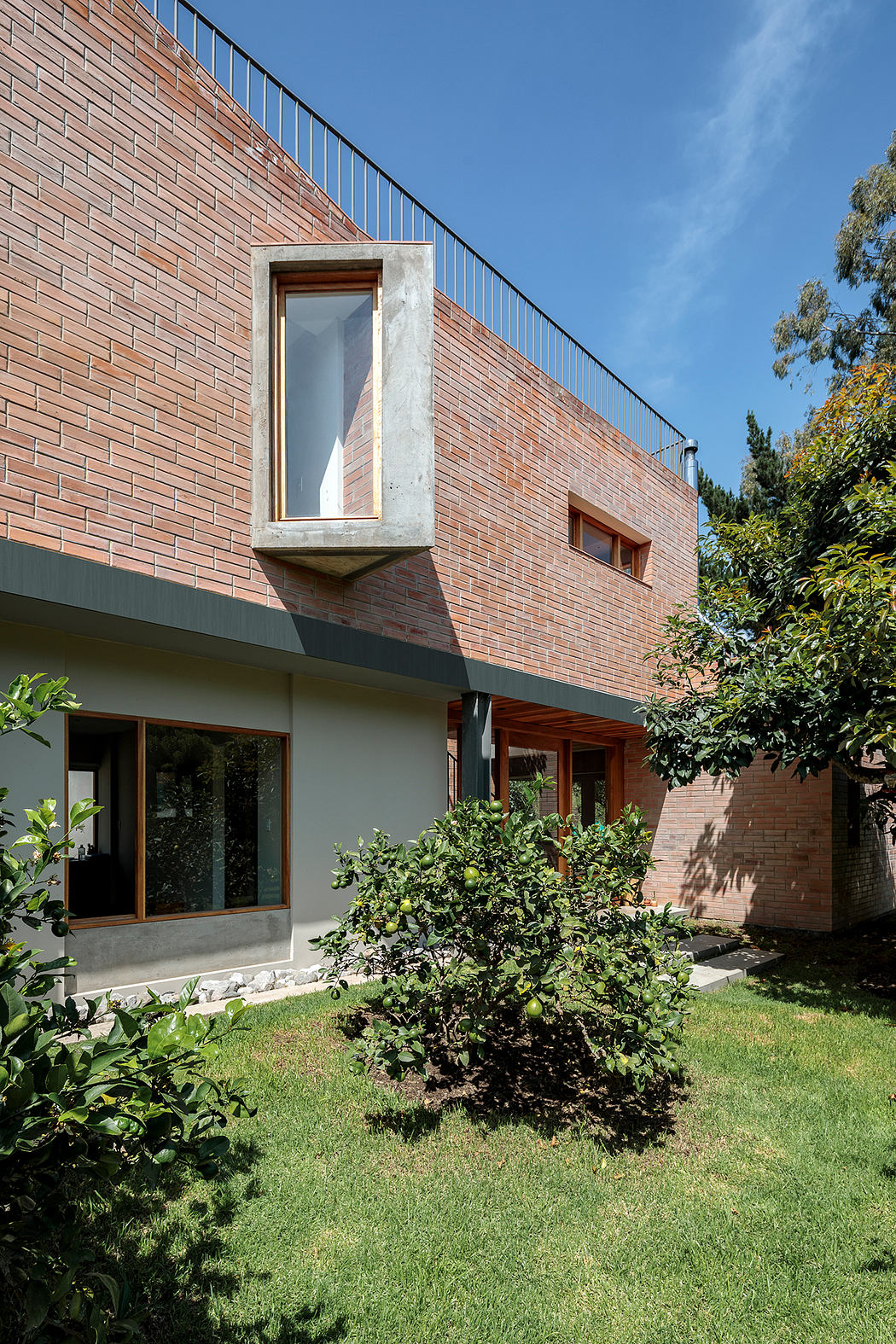 Brick facade with concrete window frames, surrounded by lush greenery and a lawn.