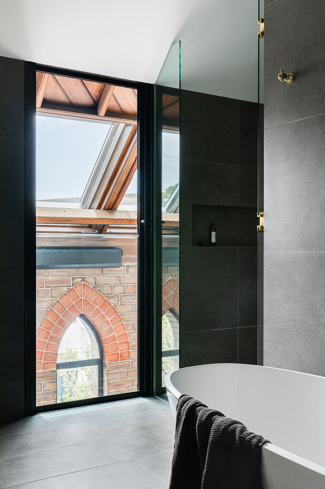 A modern bathroom with sleek black tiles, a large arched window, and a freestanding bathtub.