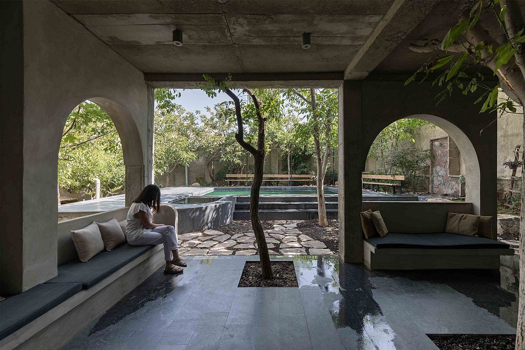 Minimalist open-air corridor with a person sitting, tree centerpiece, and cushioned