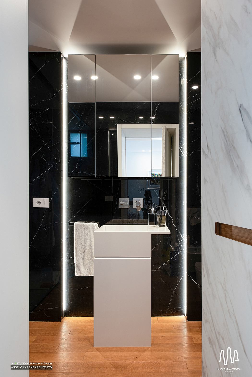 Modern bathroom with sleek black marble walls, recessed lighting, and minimalist vanity.