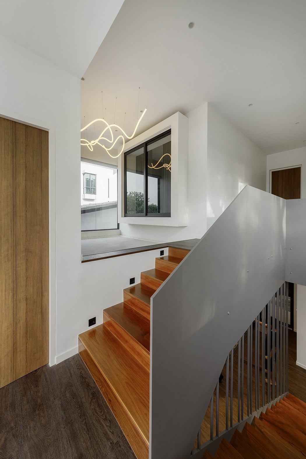 Modern staircase with wooden steps, white walls, and unique lighting fixture.