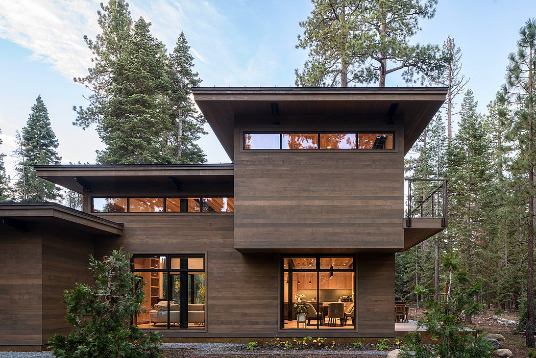 Modern two-story wooden house with large windows surrounded by trees at dusk.