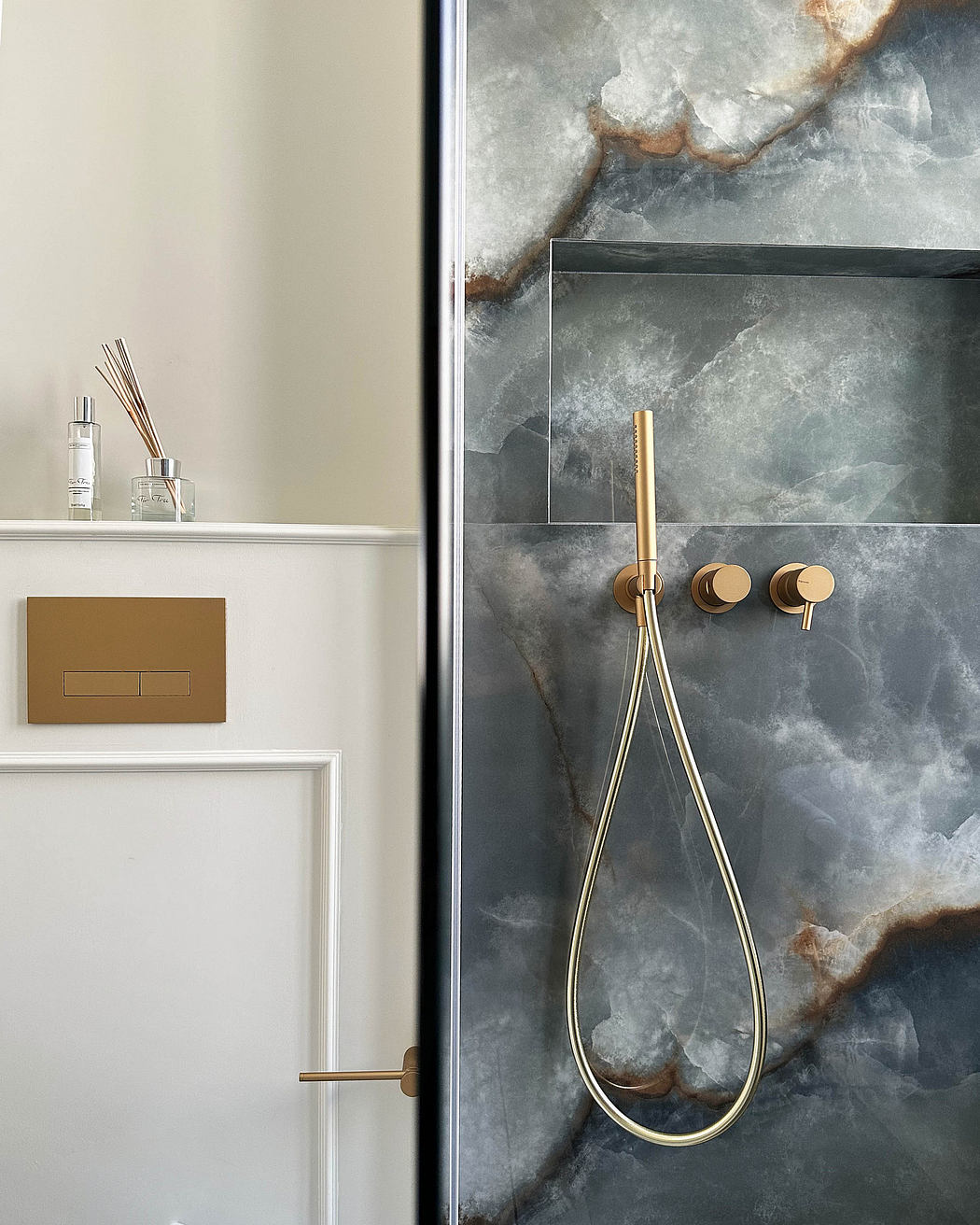 Modern bathroom with marble wall and gold shower fixtures.