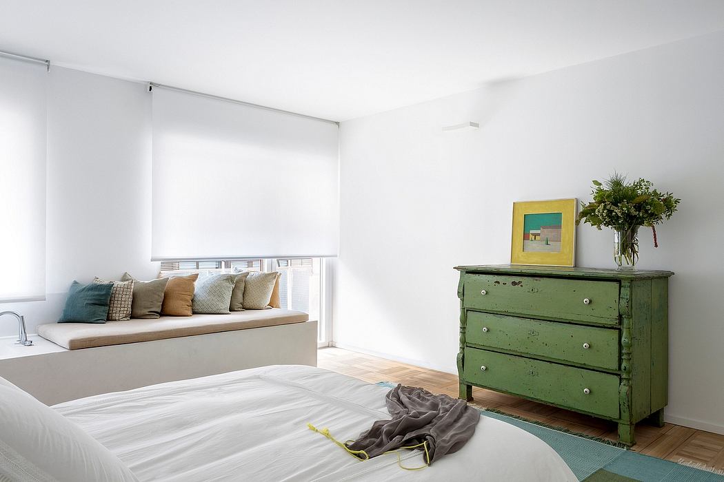 Bright, minimalist bedroom featuring a cozy window nook and a vintage green dresser.