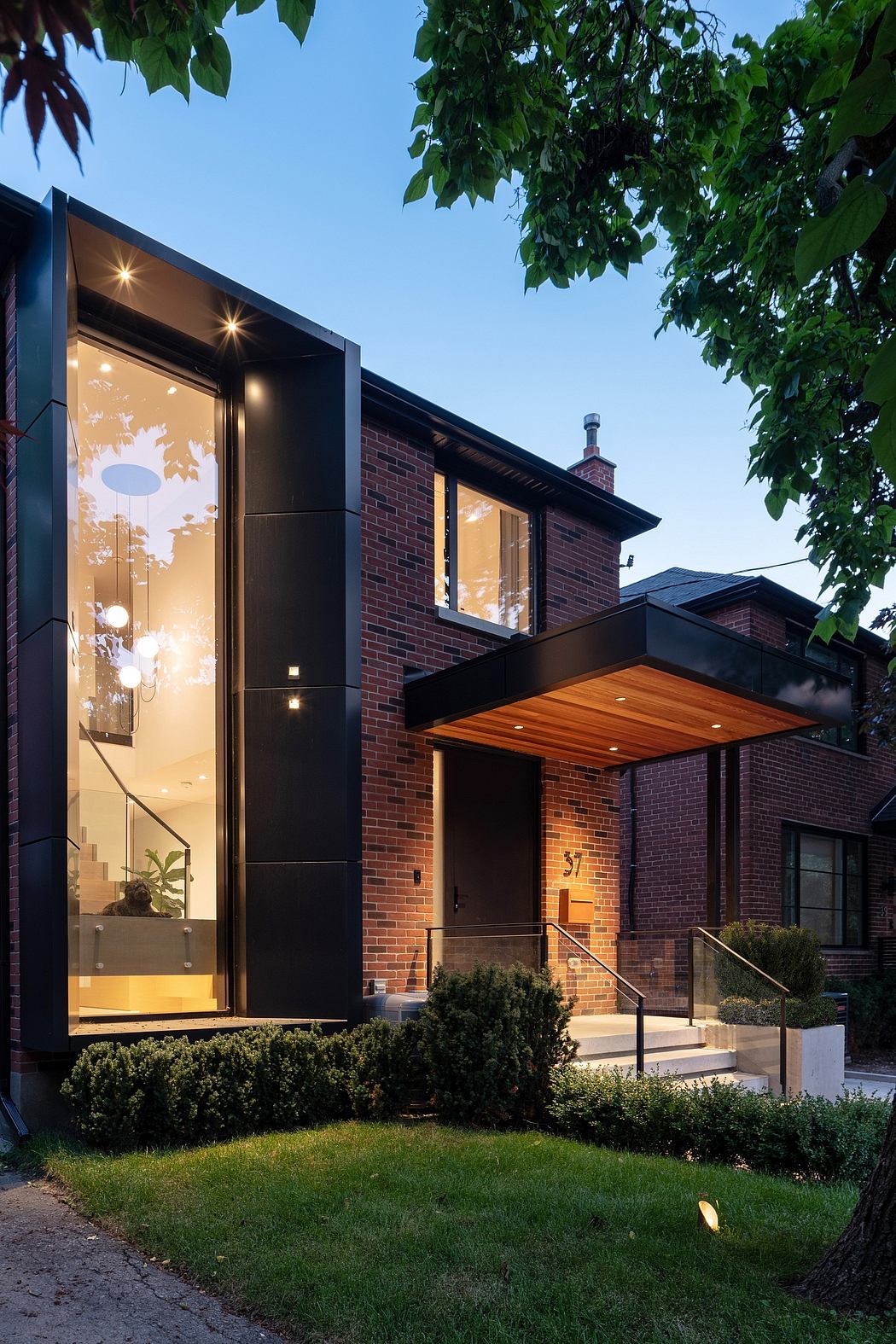 Contemporary brick house with large glass facade and lit entrance.