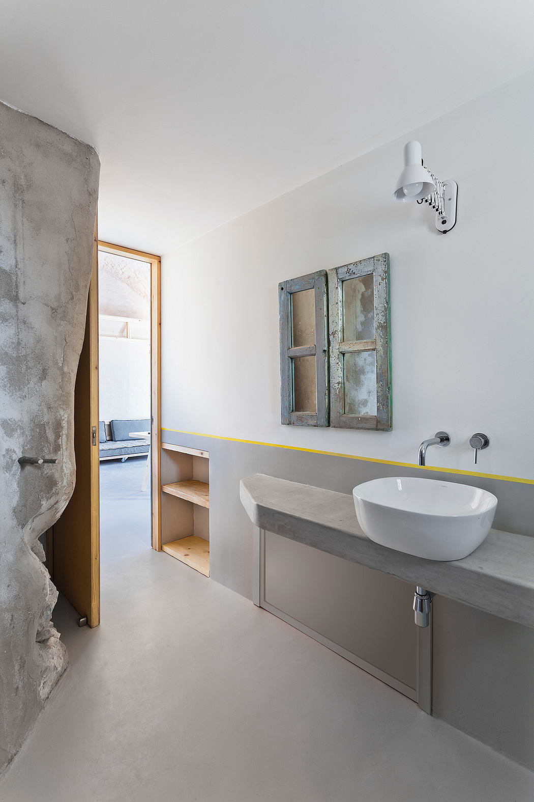 A modern bathroom with a concrete wall, wooden shelves, and a rustic mirror.