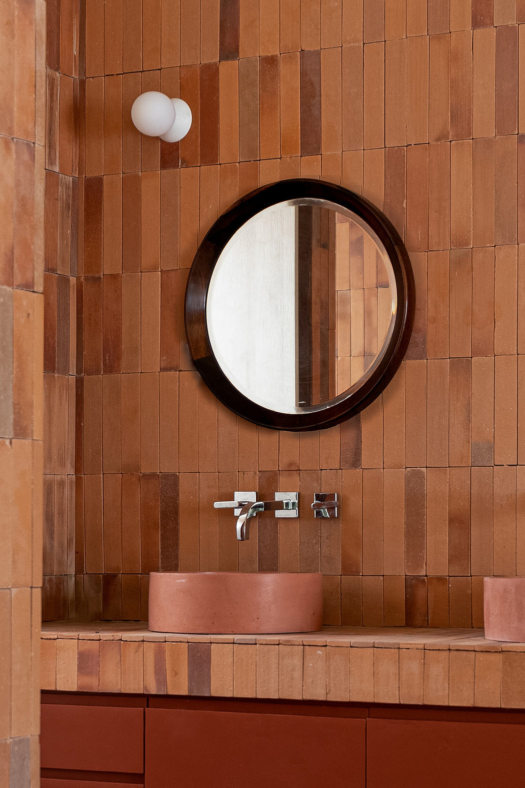Modern bathroom with terracotta tiles, round mirror, and wall-mounted sink.
