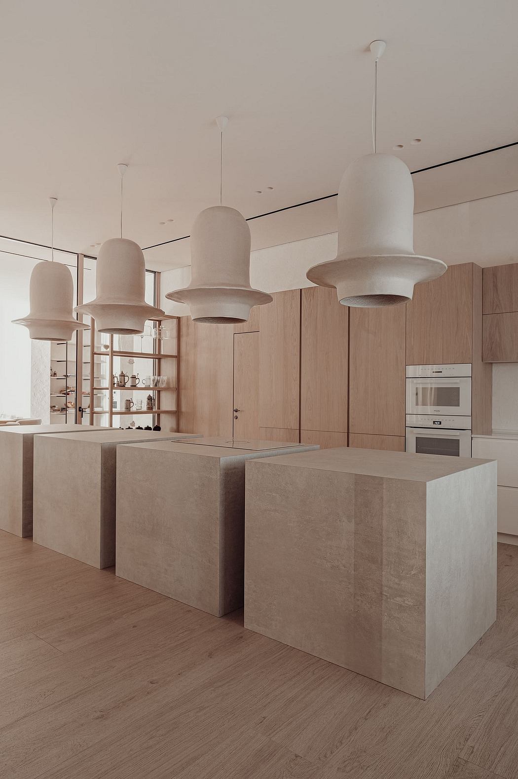 Minimalist kitchen with muted tones, concrete countertops, and suspended pendant lights.
