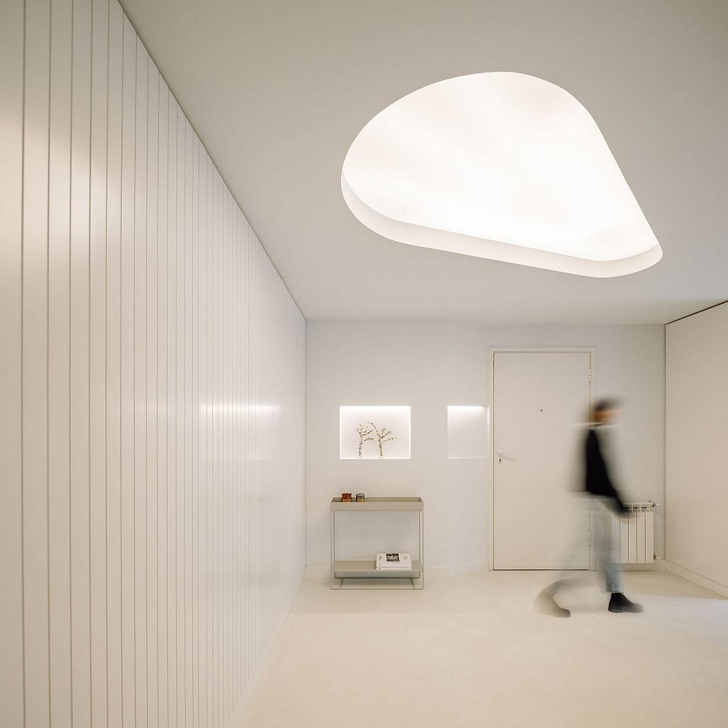 A minimalist interior with a curved white ceiling light, shelving unit, and blurred figure.