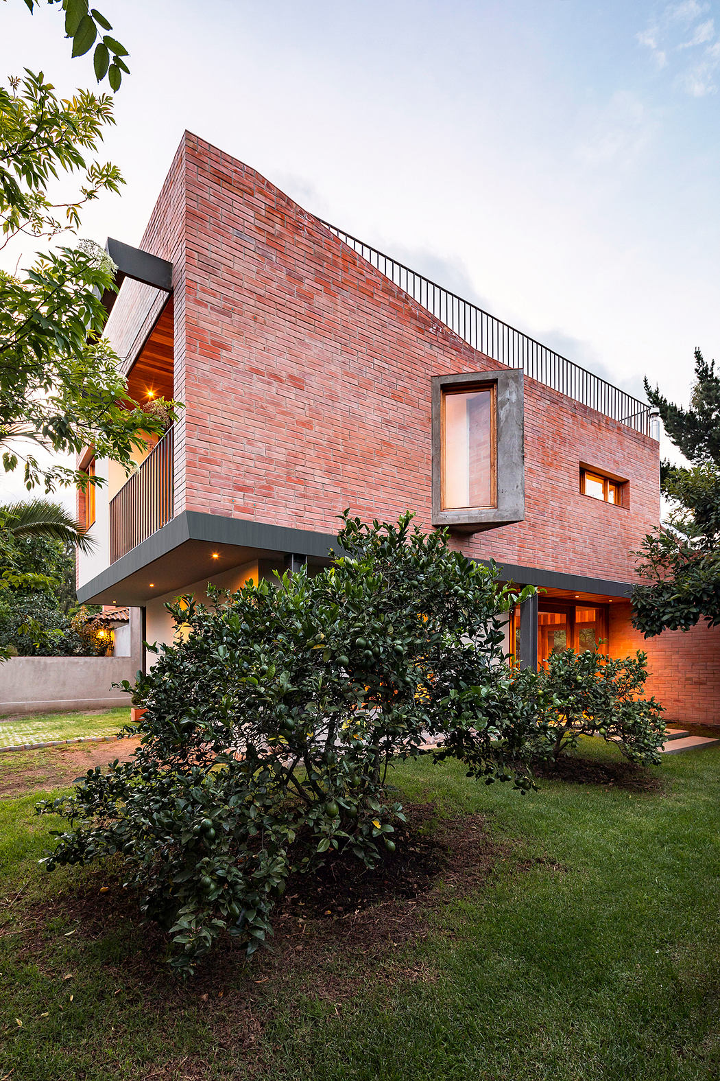 A contemporary brick building with asymmetric rooflines, surrounded by lush greenery.