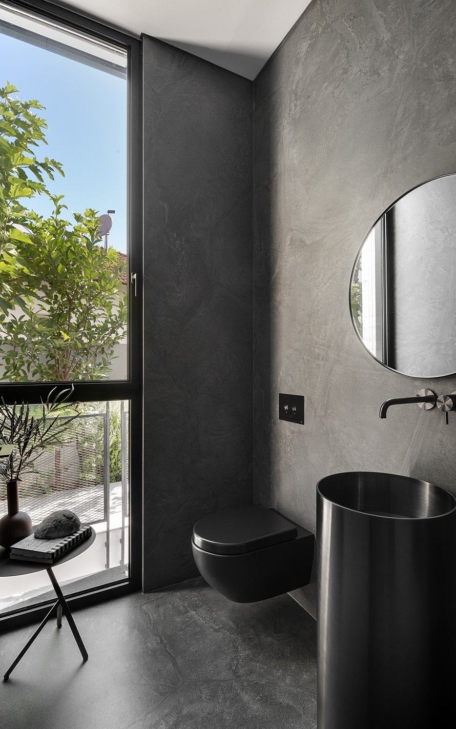 Sleek, minimalist bathroom with dark concrete walls, black fixtures, and a large window.