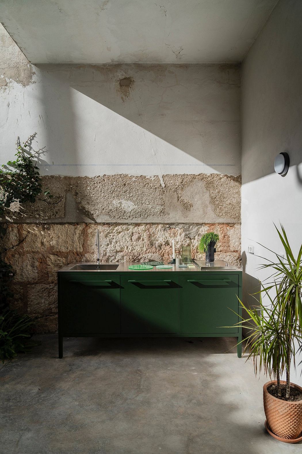 A minimalist kitchen corner with a green cabinet against a rustic stone wall, and p