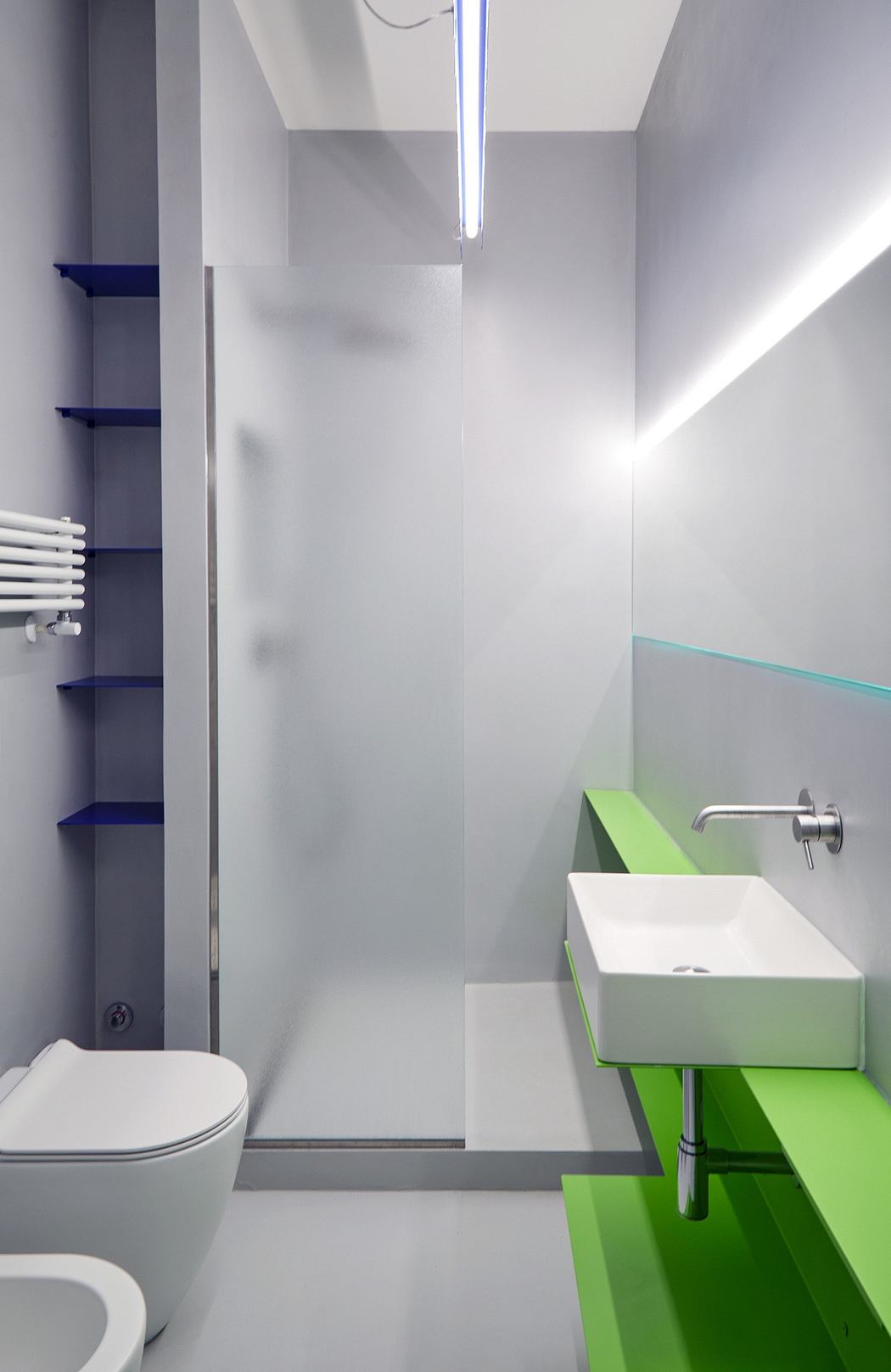 A modern bathroom with minimalist design, featuring green accents, shelves, and a glass panel.