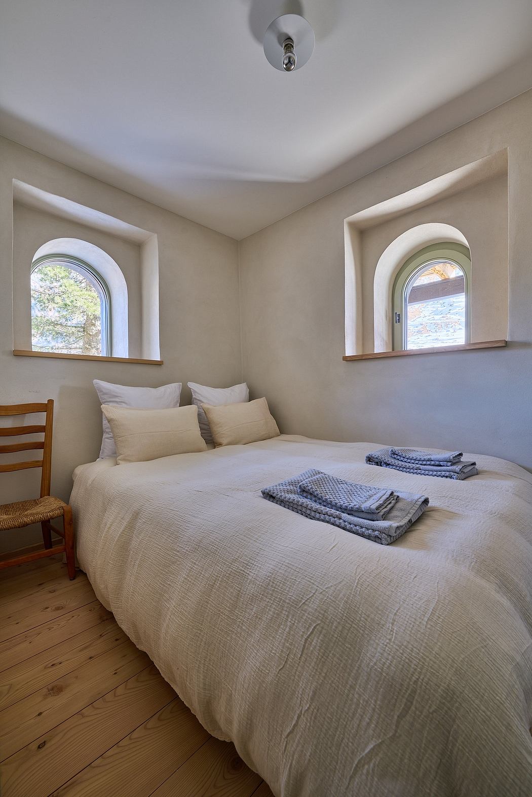 Compact bedroom with arched windows and wooden floor.