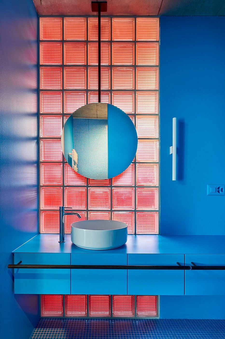 Vibrant blue and red tiled bathroom with circular mirror and minimalist vanity.