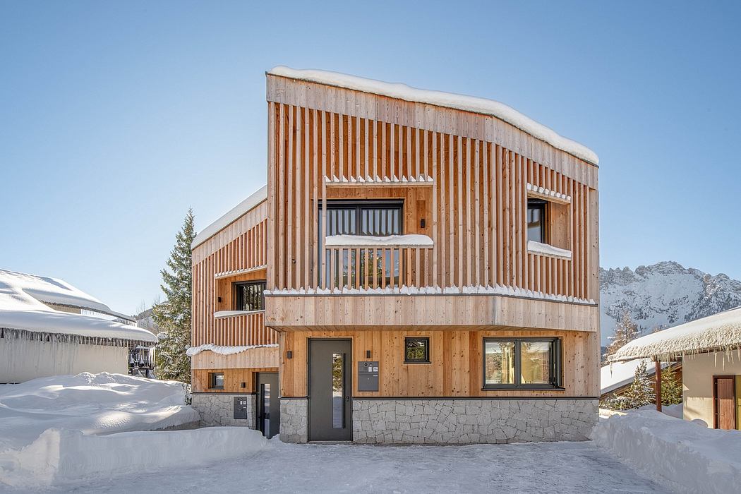 Modern wooden chalet with stone base, sloped roof, and large windows overlooking snowy landscape.