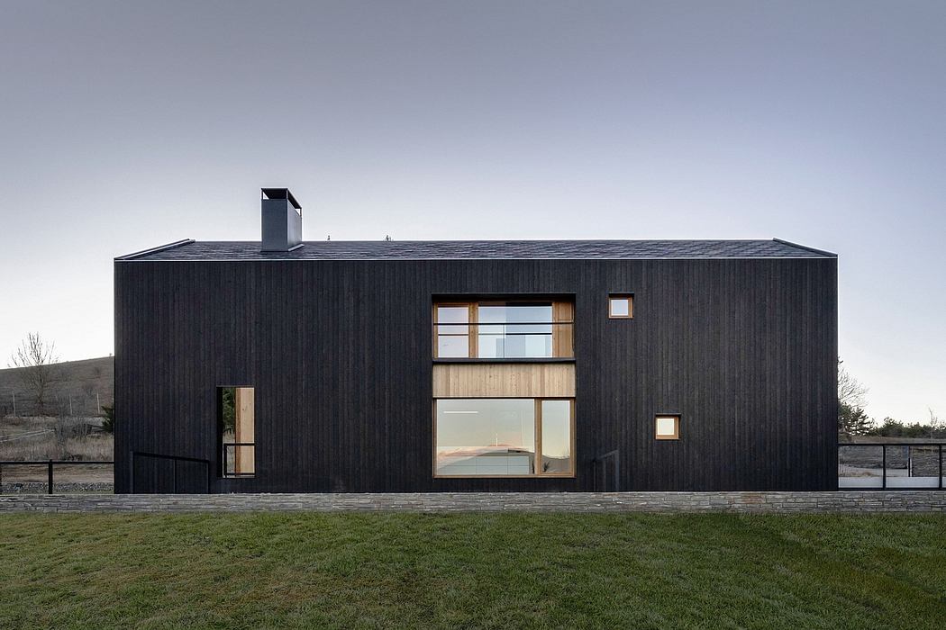 A striking modern black wooden structure with large windows, nestled in a grassy landscape.