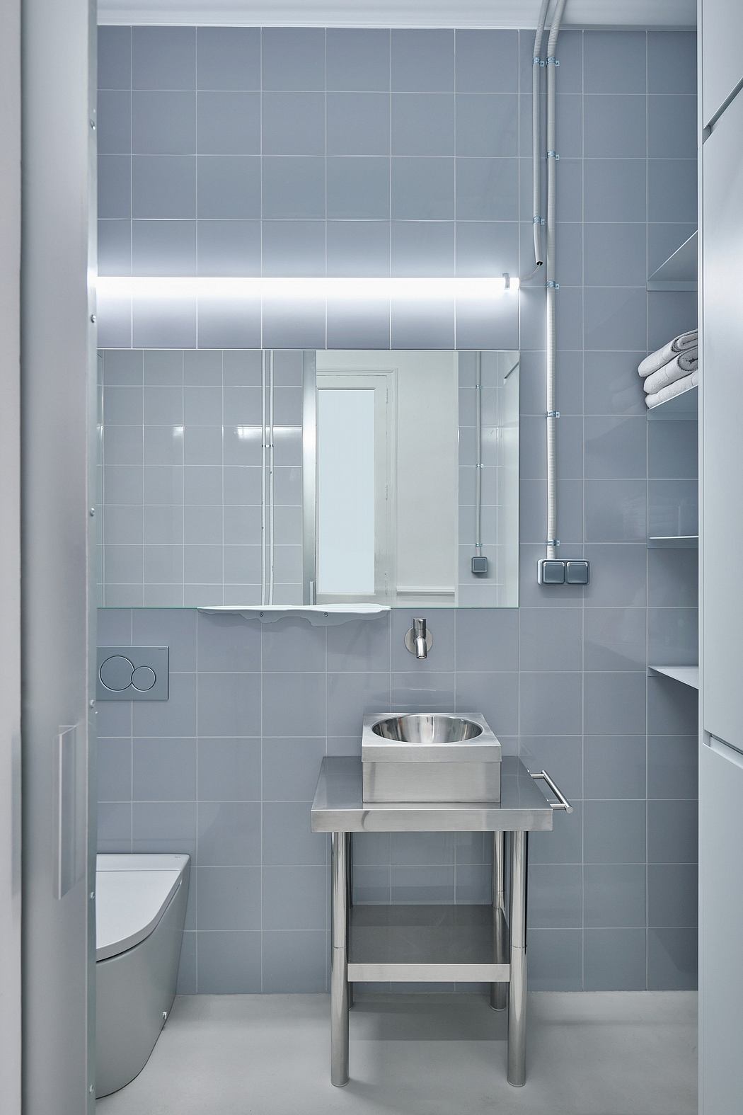 A minimalist bathroom with sleek gray tiles, a stainless steel vanity, and subtle lighting.