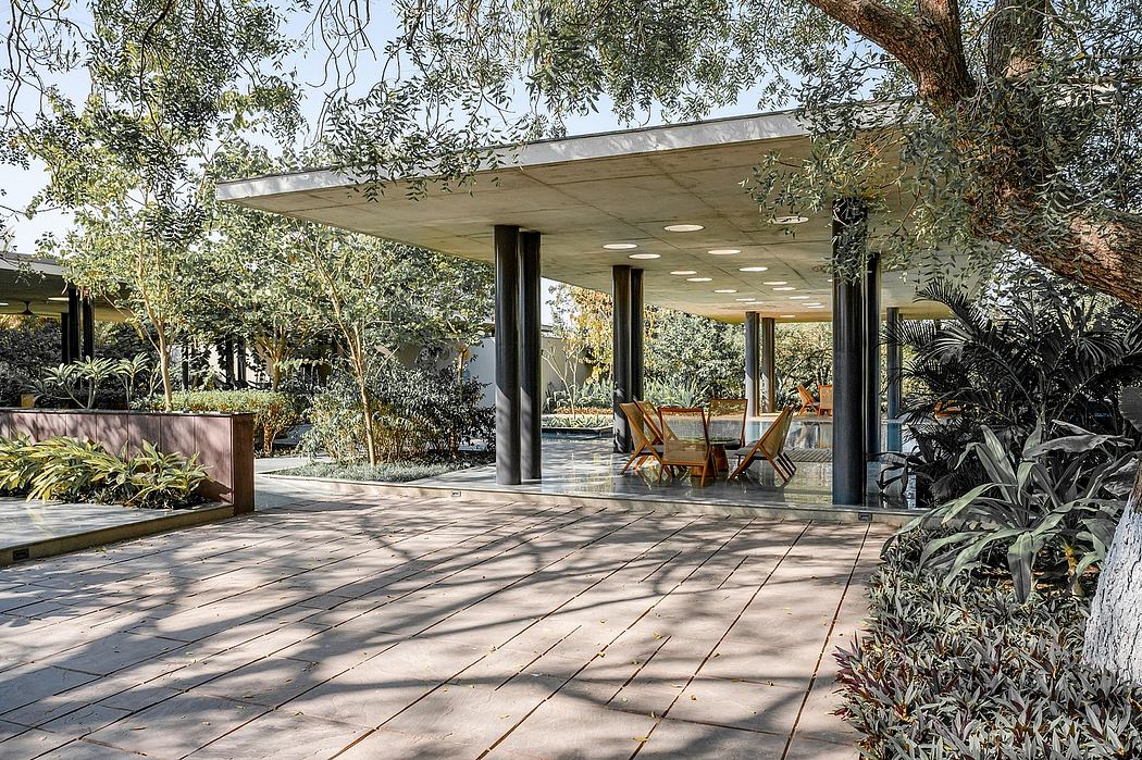 Modernist pavilion with floor-to-ceiling glass, overhanging roof, and surrounding greenery.