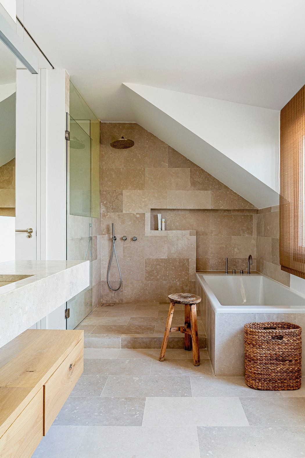 A spacious bathroom with natural stone tiles, a freestanding tub, and a wooden vanity.