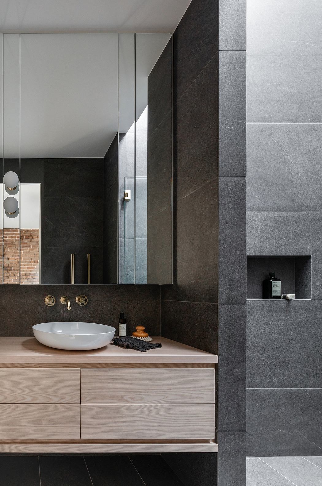 Sleek, modern bathroom with dark tiles, wood vanity, and recessed shelving.