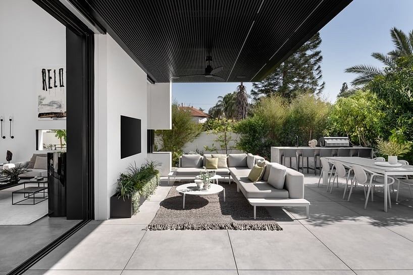 A modern outdoor living space with sleek furniture, lush greenery, and a covered patio.