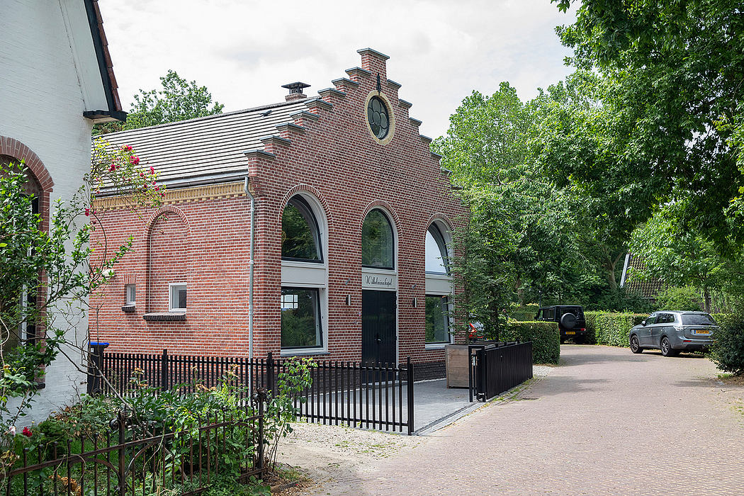 A brick building with arched windows and a decorative roofline in a wooded setting.
