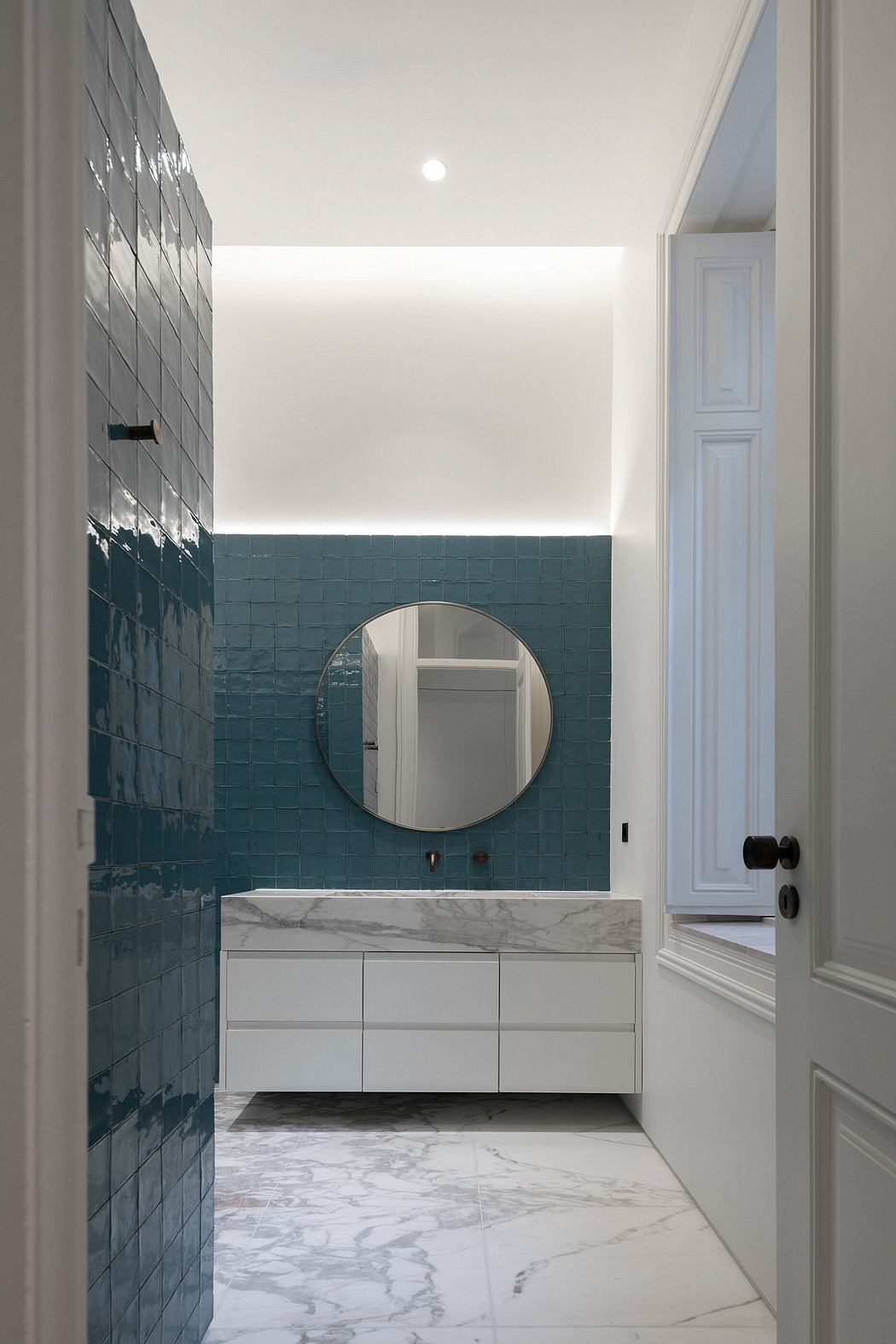 Contemporary bathroom with teal tiles, marble floor, and white vanity.