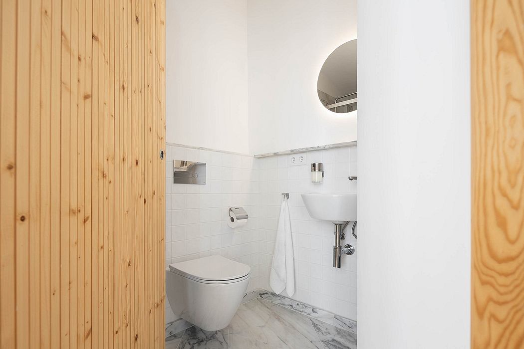 Modern bathroom with wooden door, white fixtures, and marble floor.