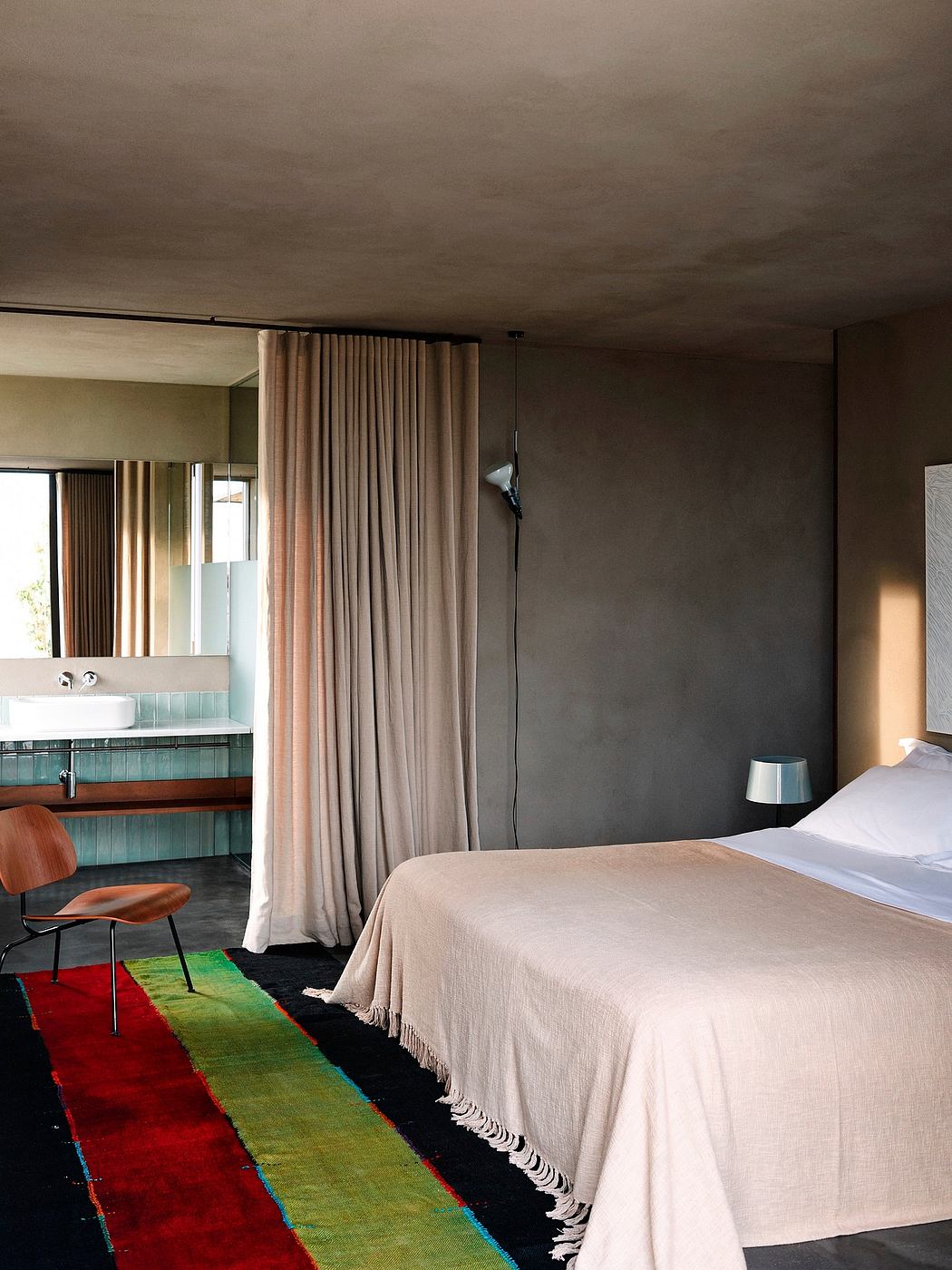 Modern bedroom with neutral colors, exposed concrete, and colorful rug.