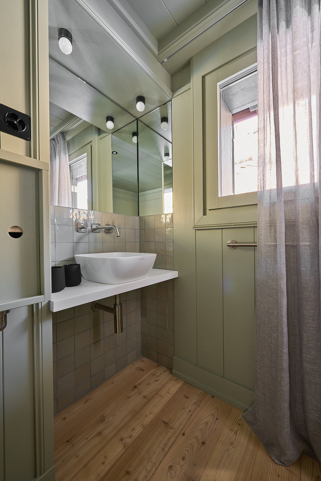 A narrow bathroom with green walls, wooden floor, a white sink, and a