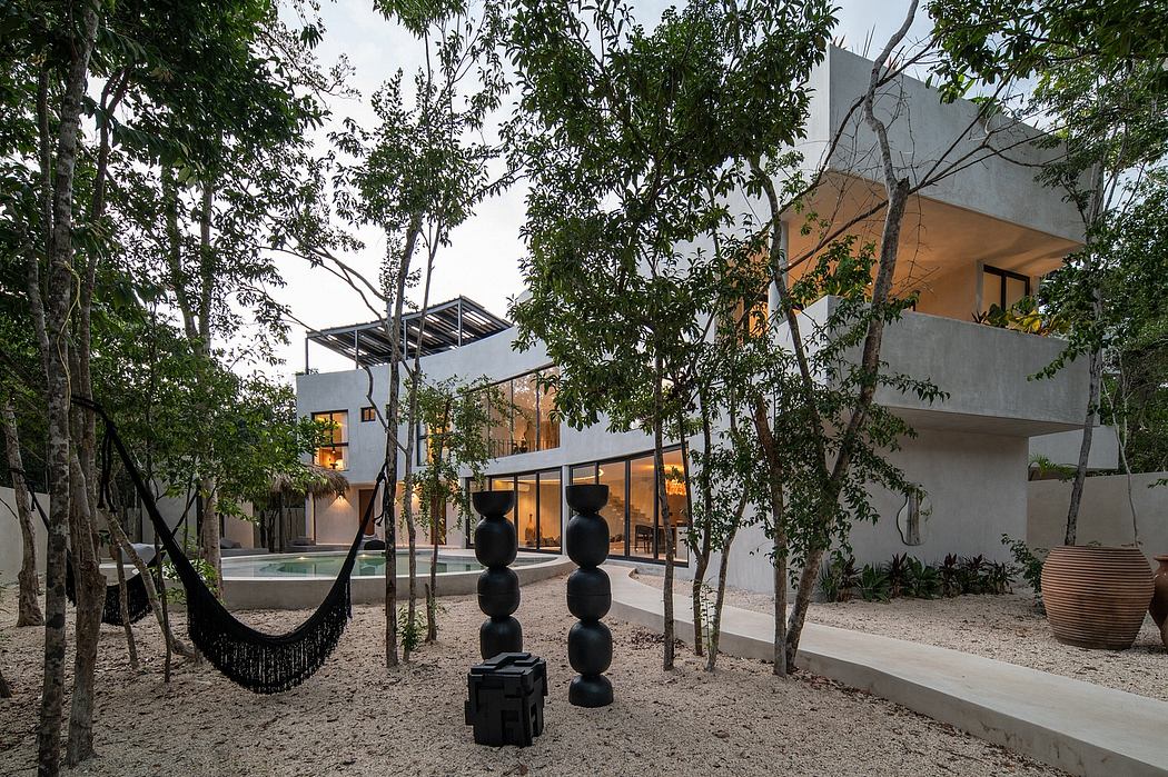 Modern house with an outdoor hammock, trees, and artistic sculptures.