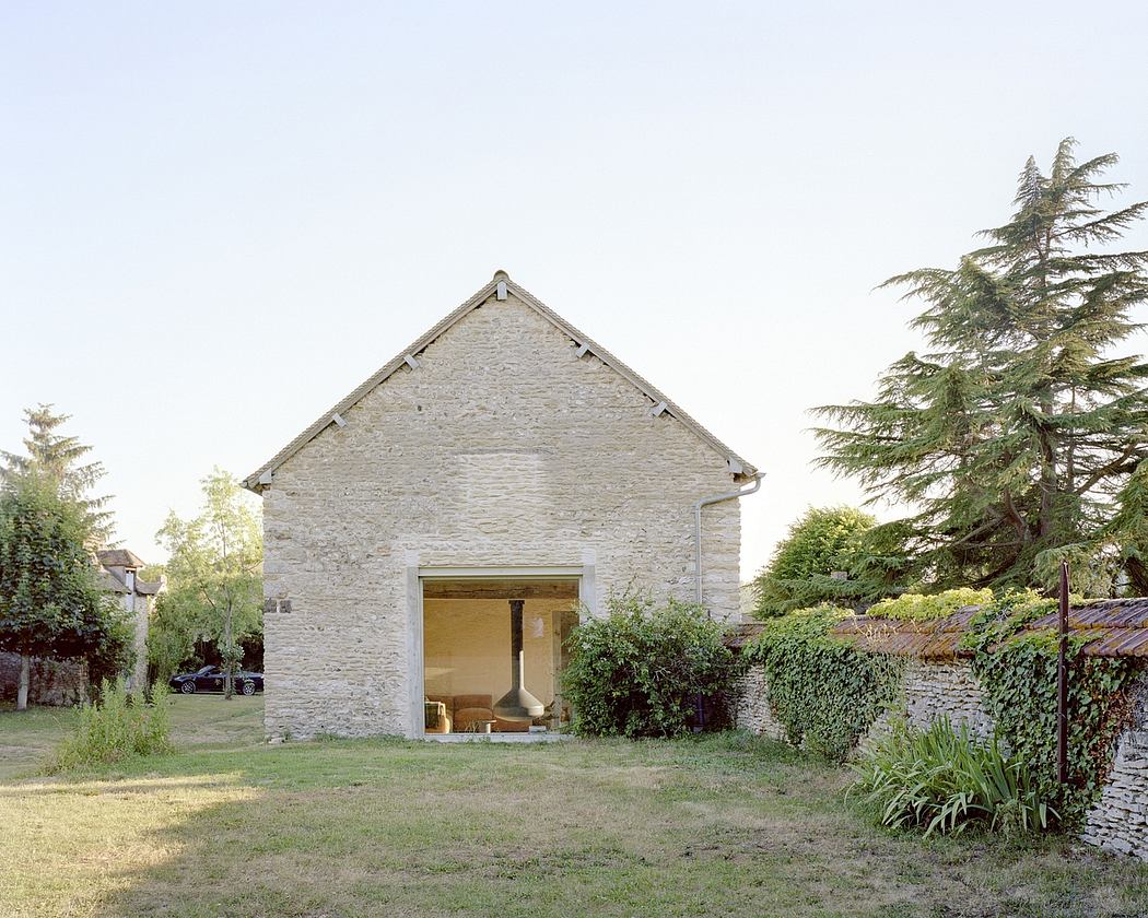 Stone building with open glass doors leading to interior, in a green garden.