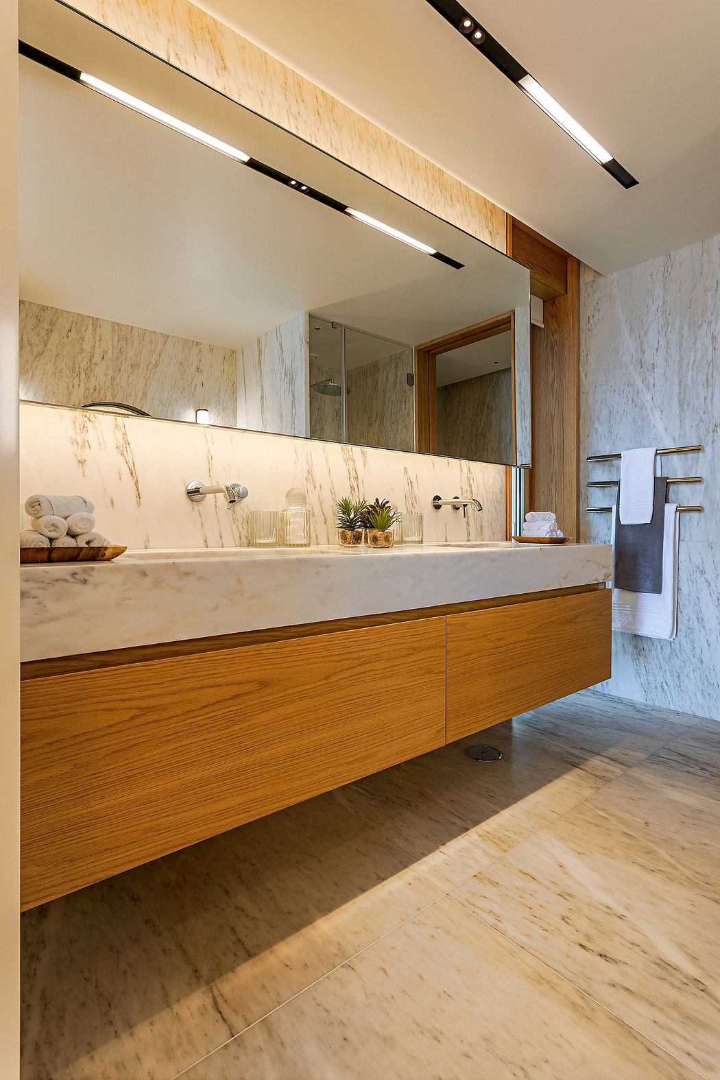 Modern bathroom with wooden vanity, marble walls, and lit mirror.