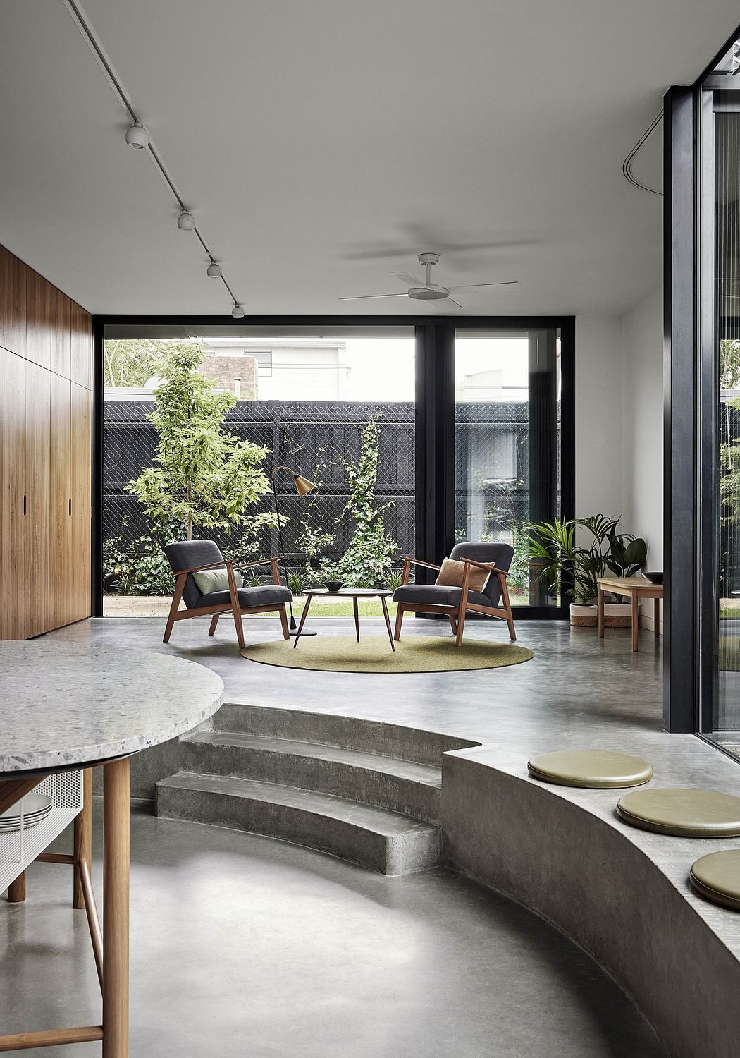 Serene indoor-outdoor living space with concrete steps, plush seating, and lush greenery.