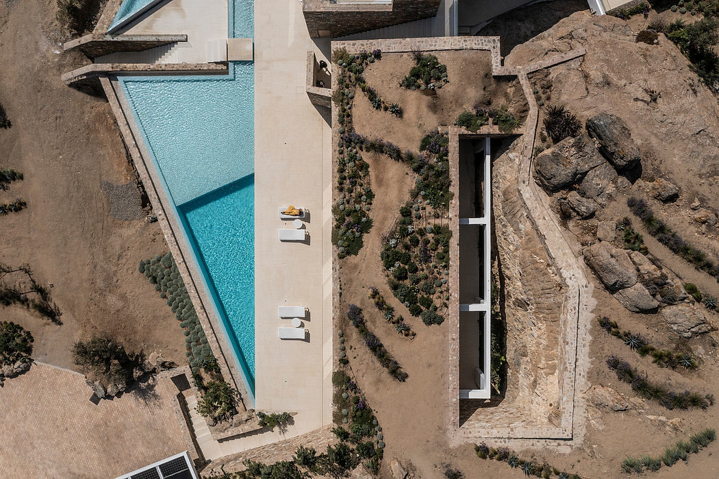 Aerial view of a sleek pool beside a contemporary home on rugged terrain.