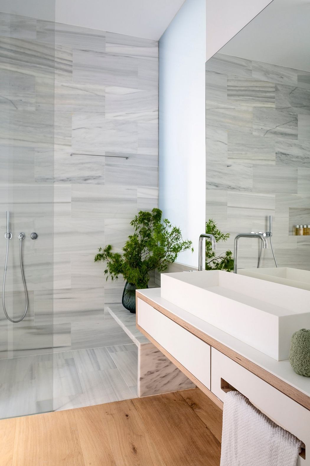 Sleek, modern bathroom design with contrasting marble tiles, minimalist vanity, and greenery accent.