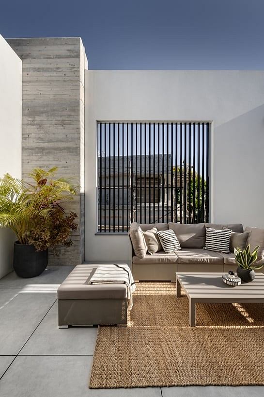 Minimalist outdoor patio with concrete walls, striped metal screen, and natural furnishings.