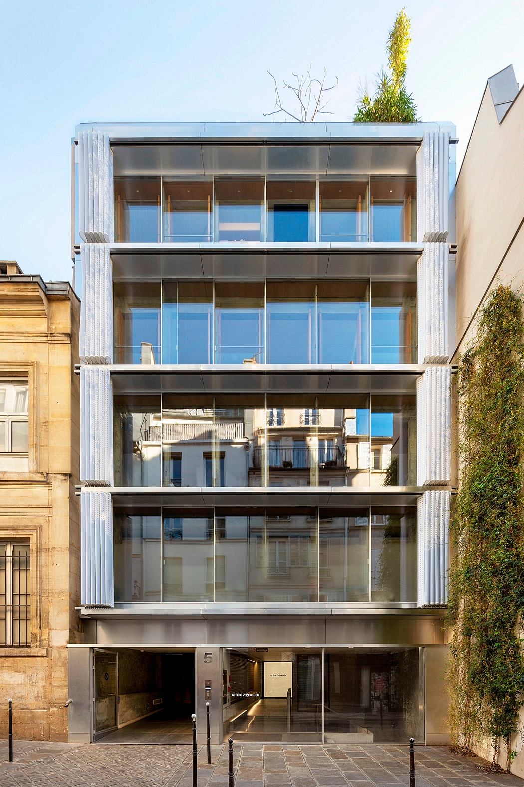 A modern glass-fronted building with clean lines, balconies, and a plant-covered rooftop.
