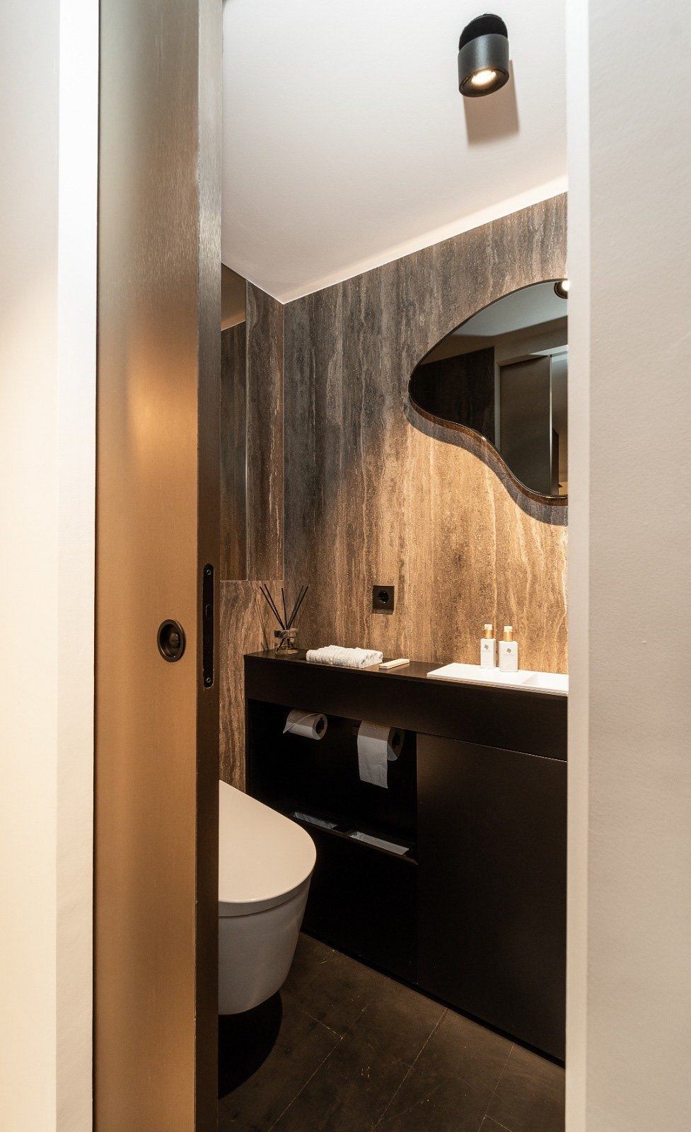Contemporary bathroom with rustic wall, floating vanity, and sleek fixtures.