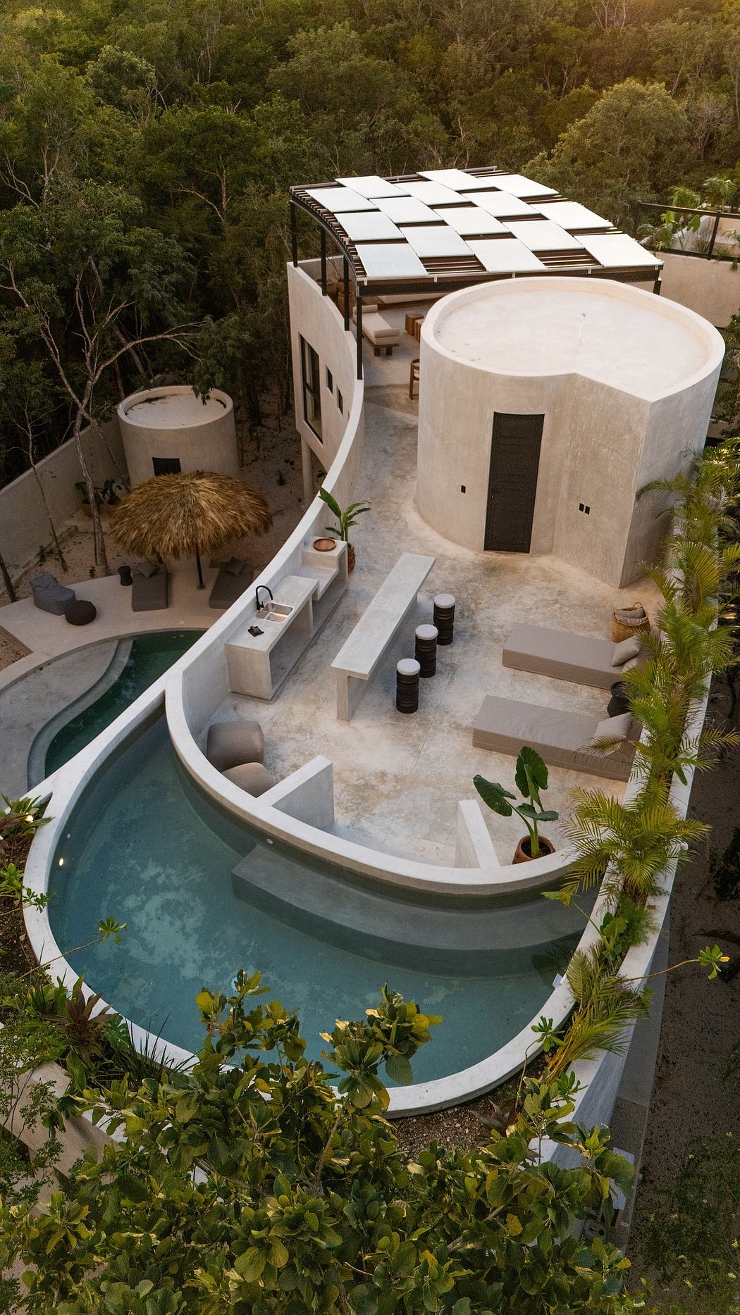Contemporary villa with curved design and rooftop solar panels amidst lush greenery.