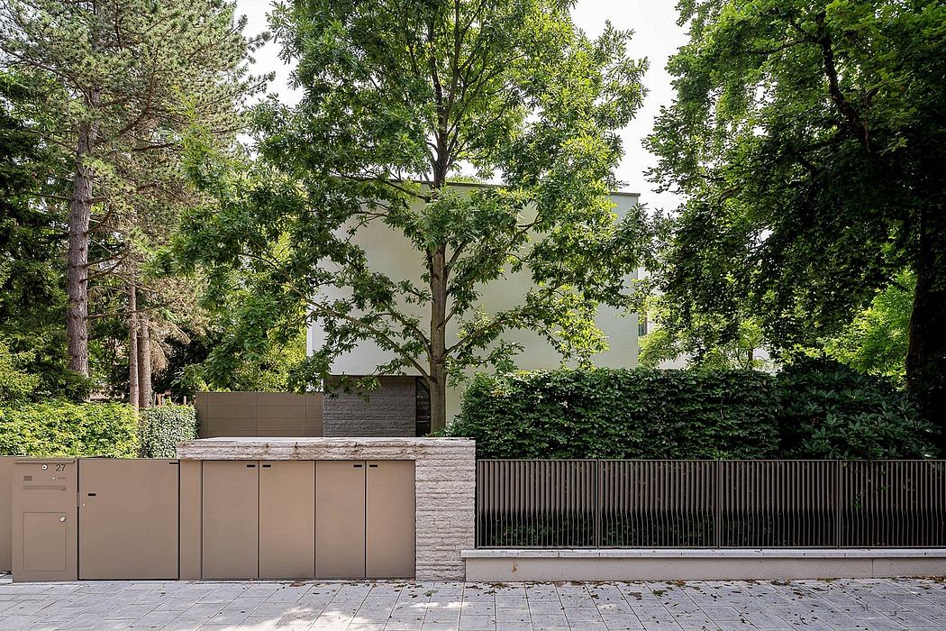 A modern, minimalist building with gray facade, surrounded by lush greenery and stone wall.