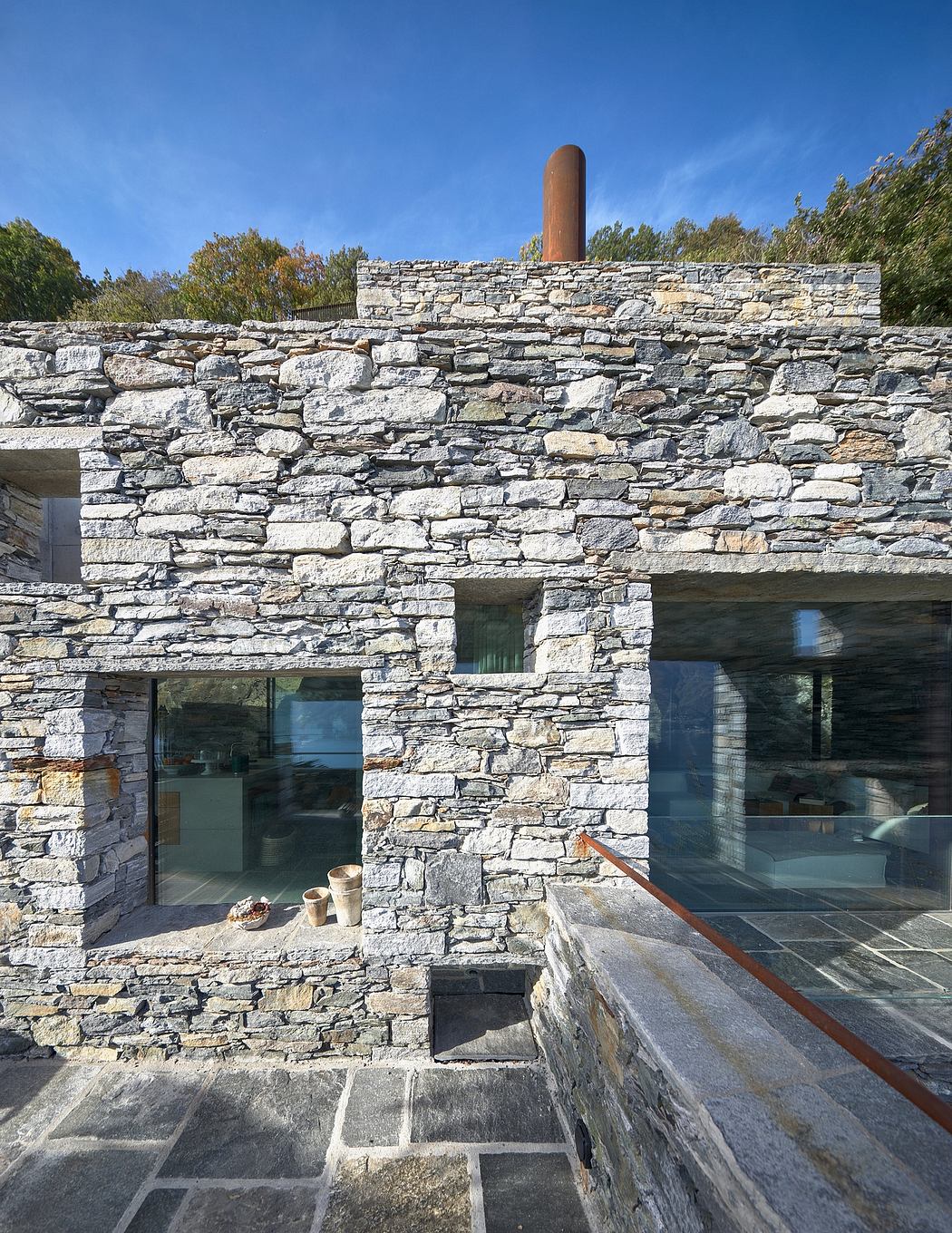 Modern stone building with large windows and a chimney.