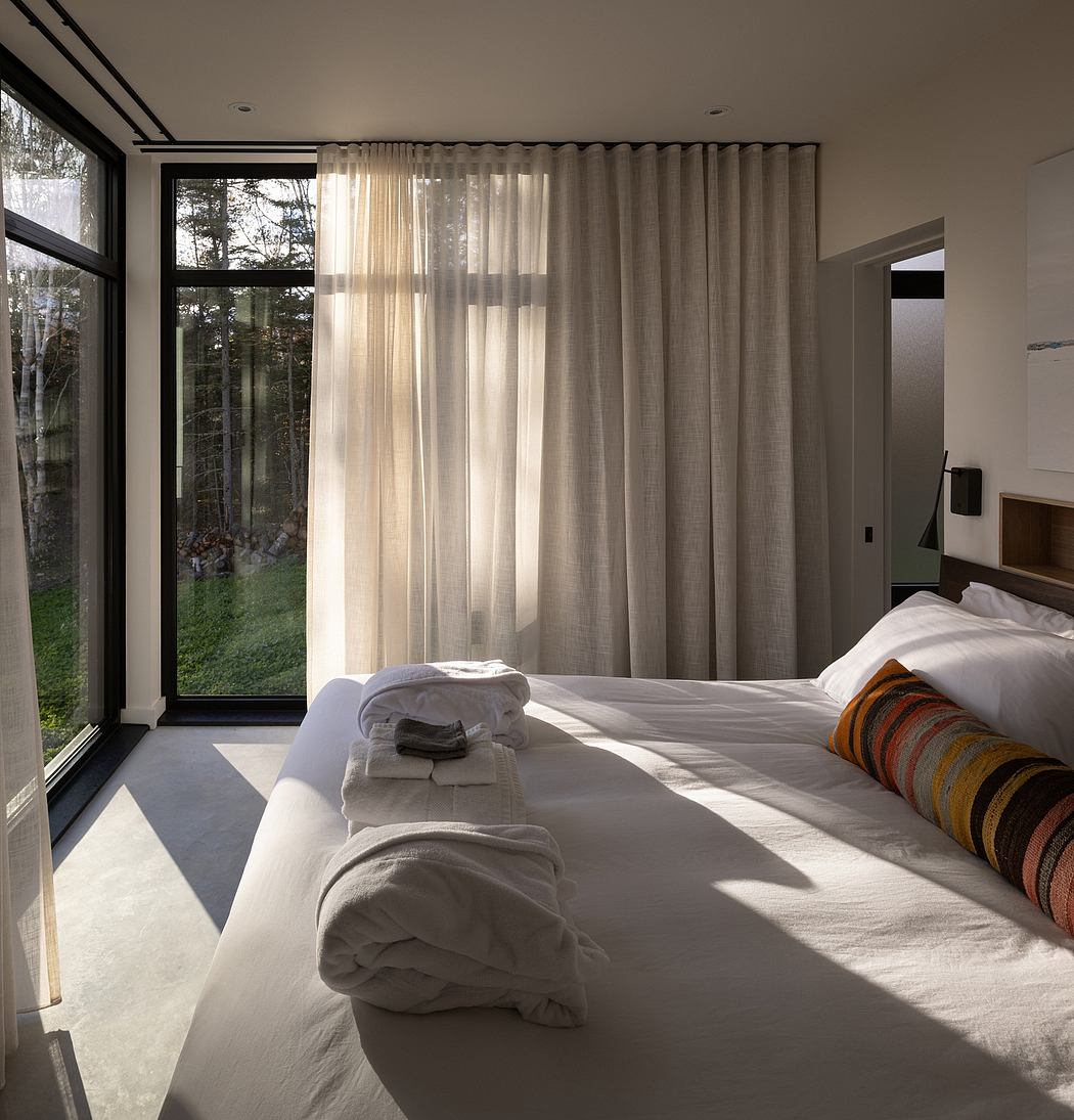 Modern bedroom with large window, sheer curtains, and sunlight filtering through.