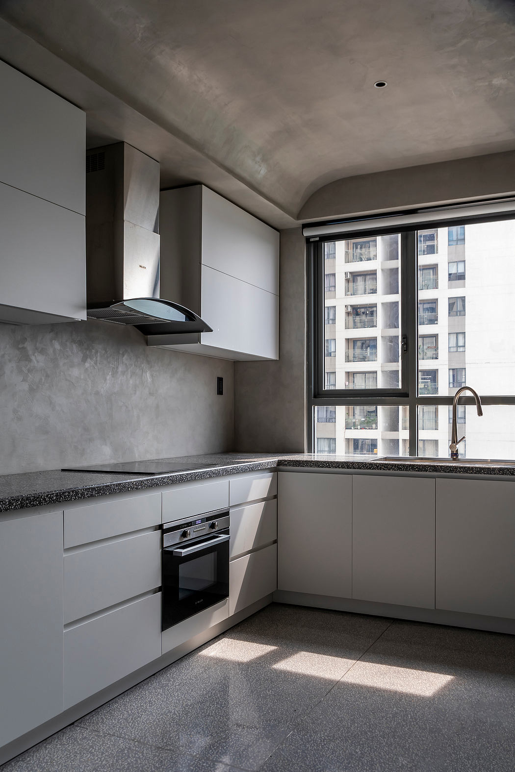 A modern kitchen with minimalist gray cabinets, sleek appliances, and a large window offering city views.