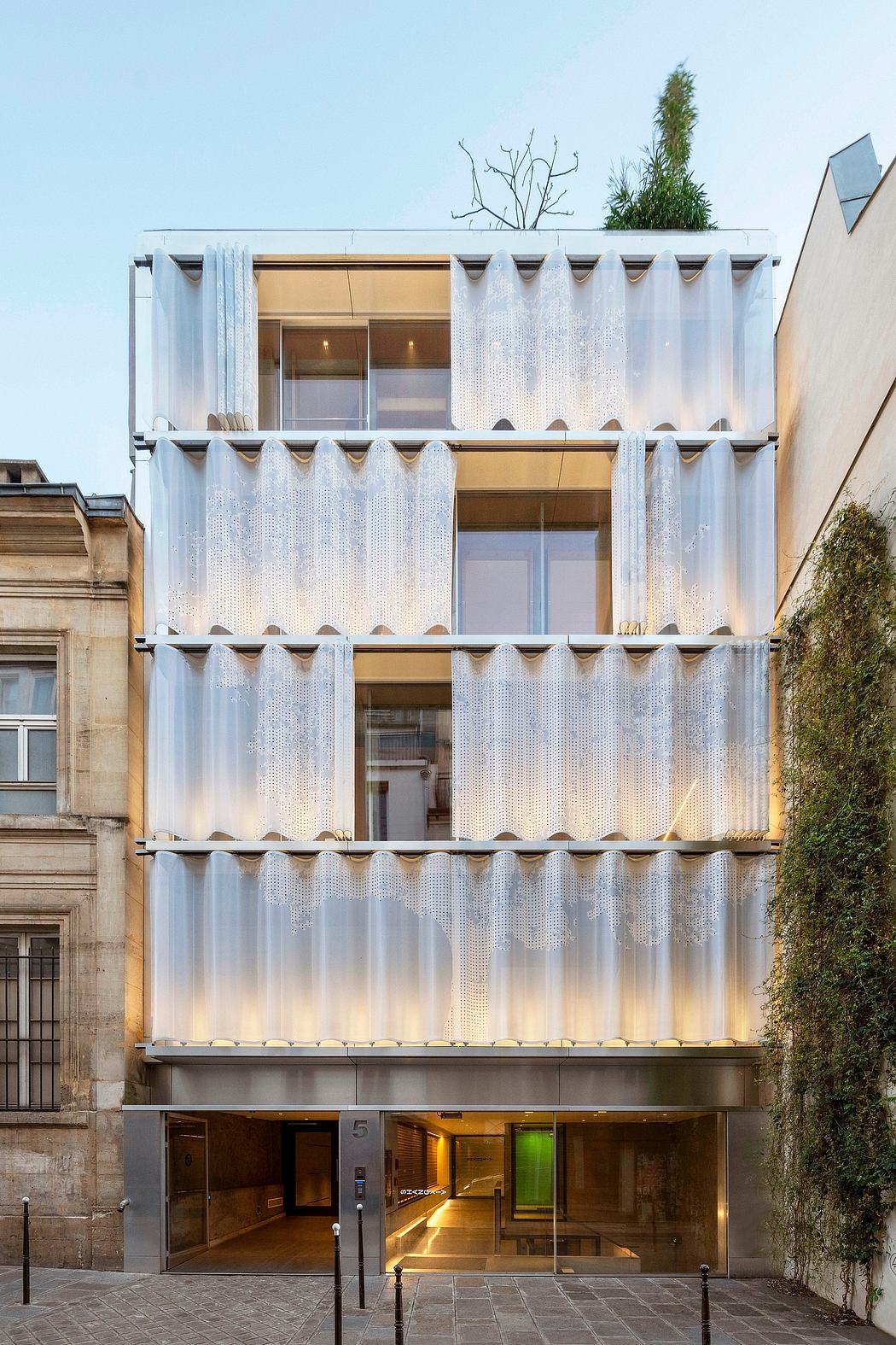 Striking modern building façade with intricate curtain-like metal panels and greenery accents.